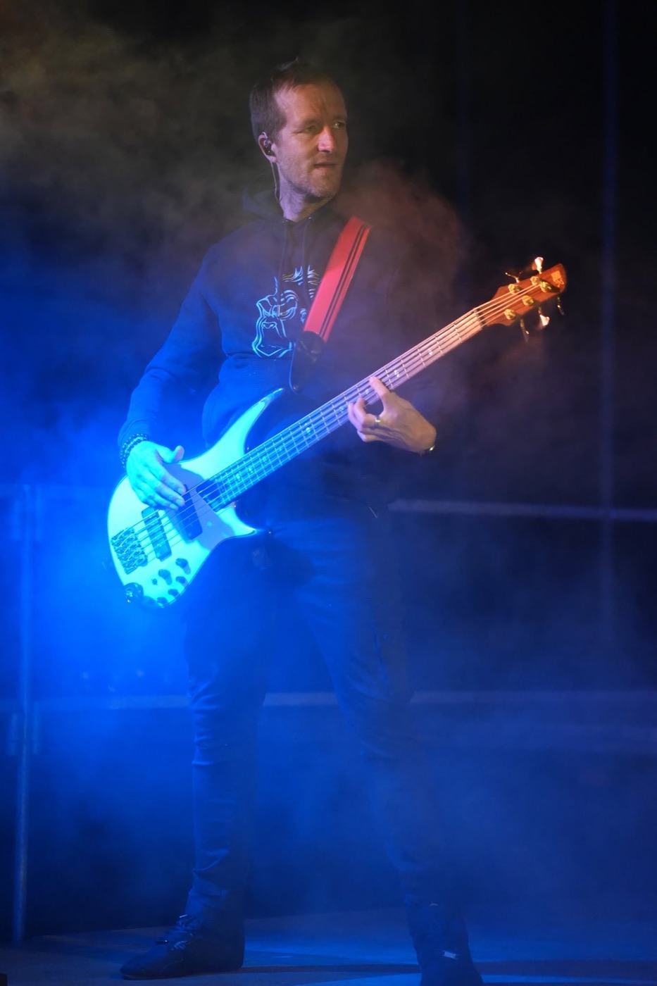 Bassiste de PINK GORILLA jouant une basse blanche au milieu des lumières bleues et de la fumée de scène.