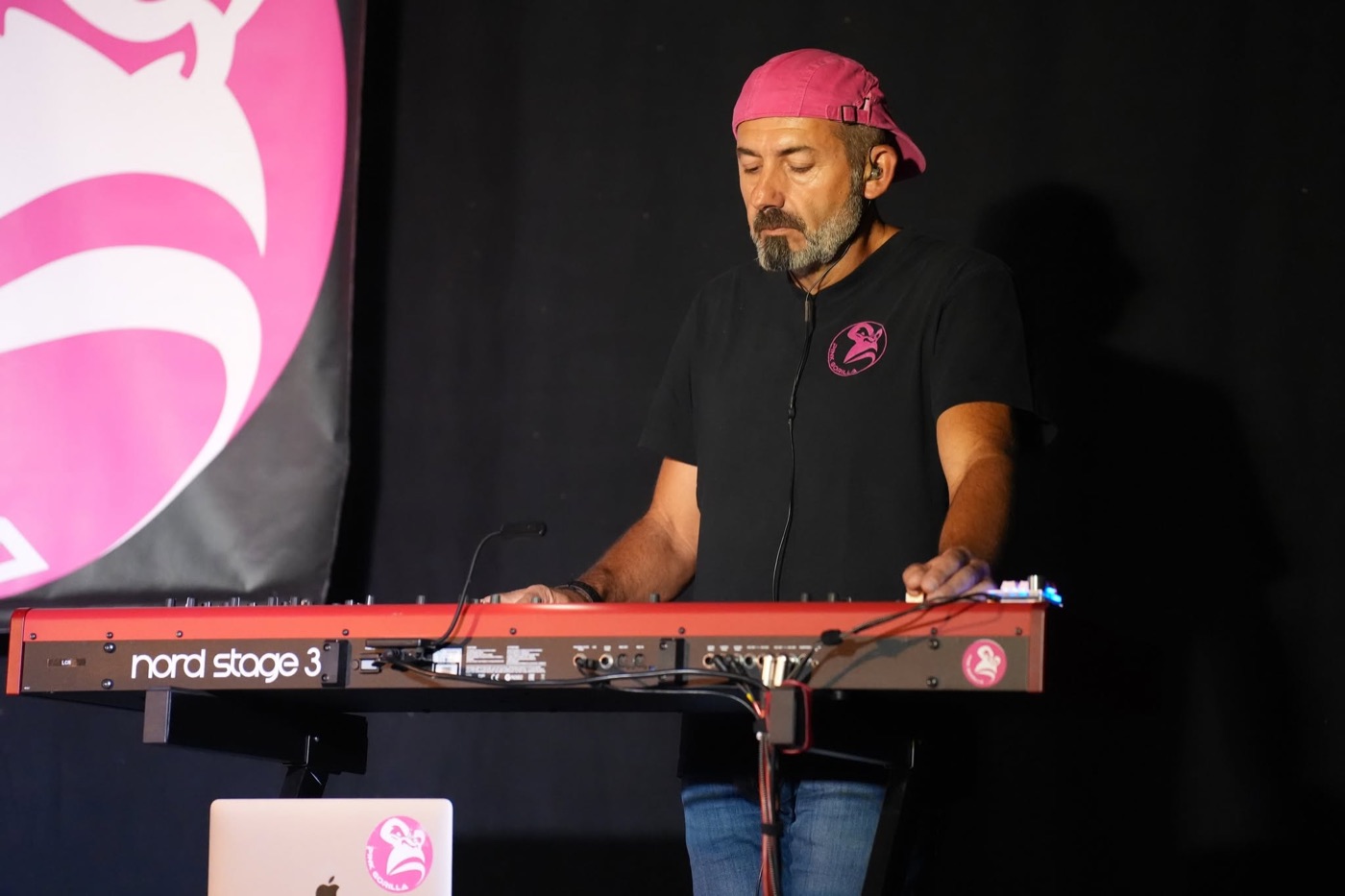 Claviériste de PINK GORILLA jouant sur un clavier rouge, avec le logo rose du groupe en arrière-plan.